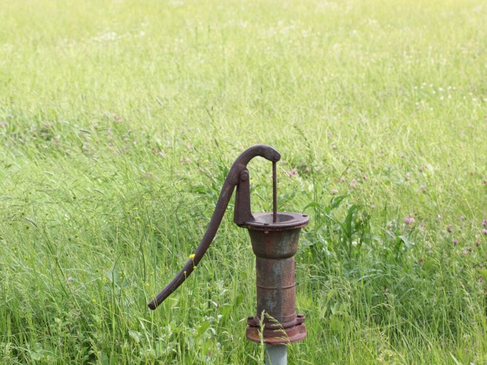 An old, rusted well pump in a green grassy field.