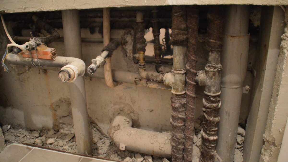 Exposed and corroded plumbing behind a partially demolished wall addresses plumbing issues.