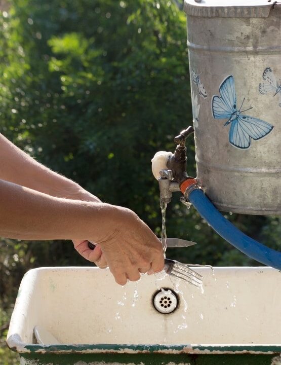 Person washing hands at an outdoor sink, consuming 40 gallons of water from a container with a butterfly sticker.